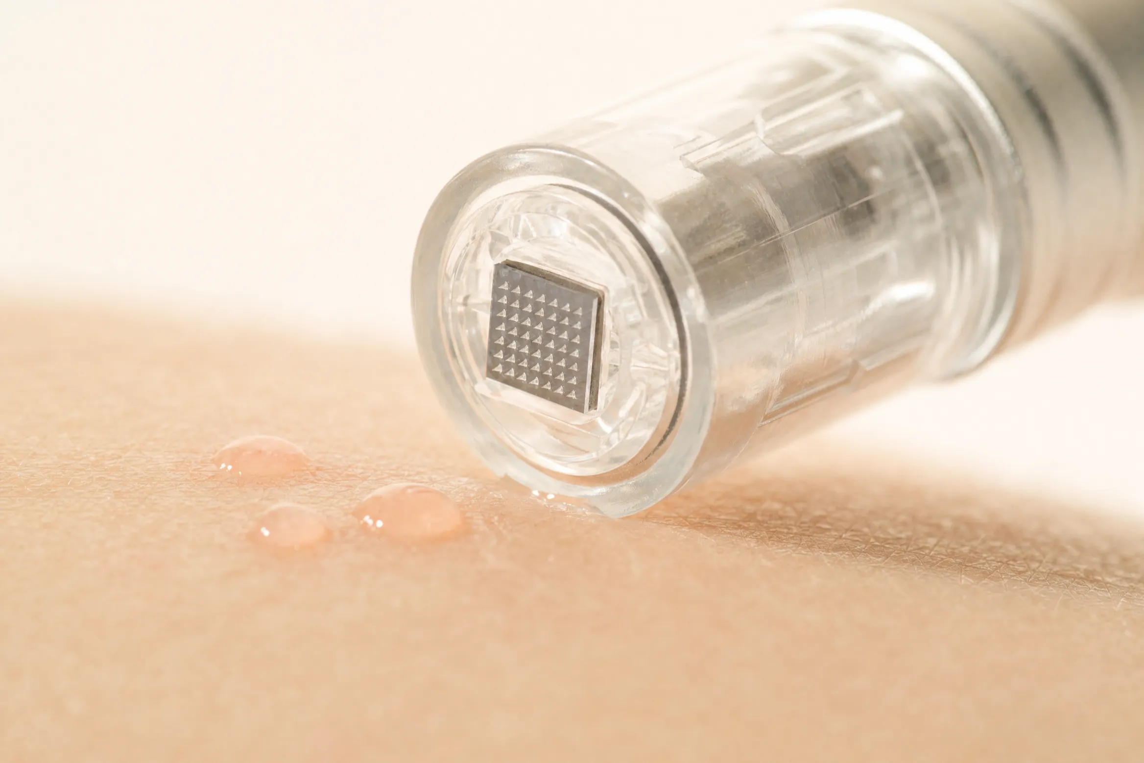 Nadelfreies Nanoneedling: transparente Feather-Touch-Kartusche mit Nano-Pyramiden-Raster liegt auf der Haut, daneben feine Serum-Tropfen