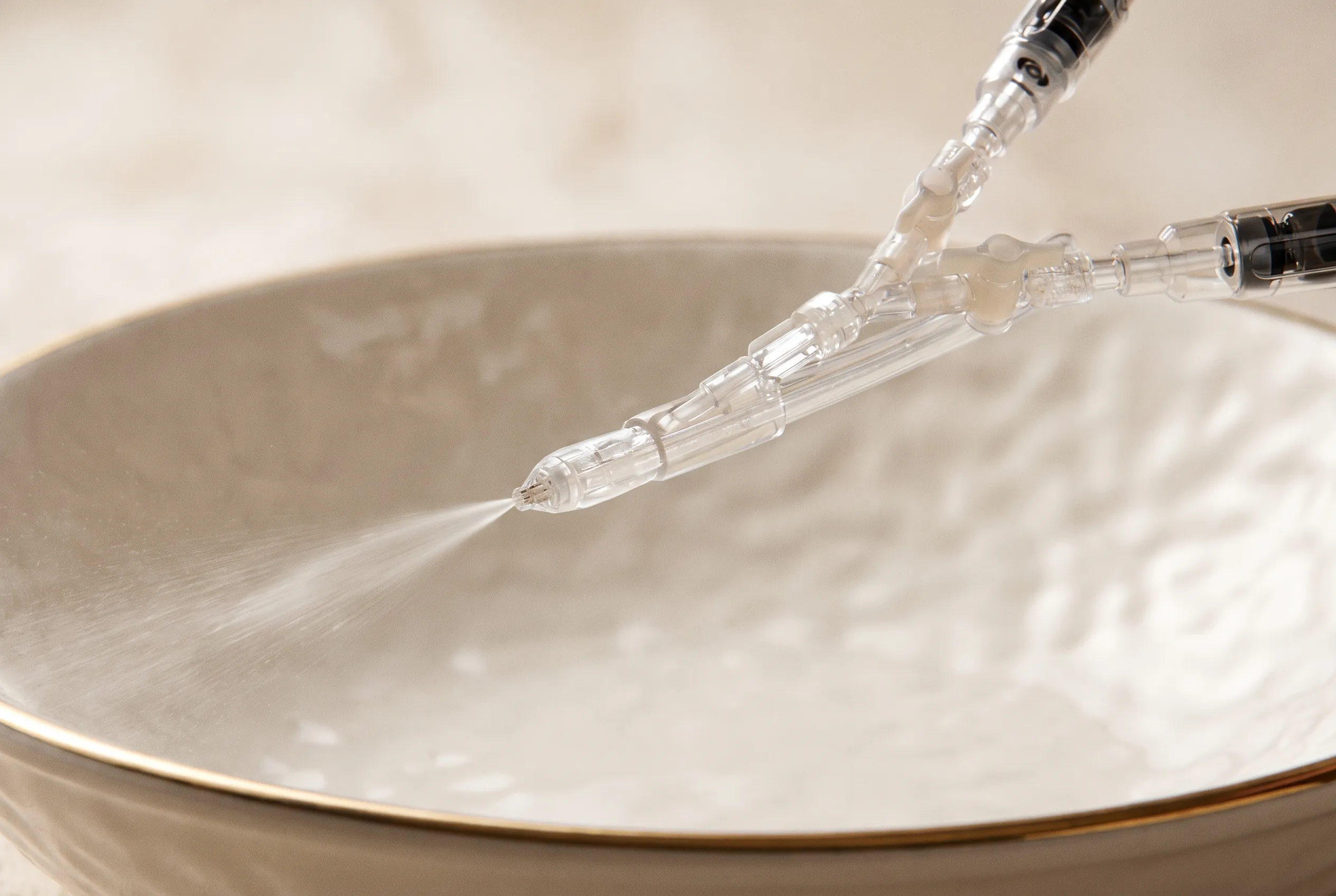 JetPeel-Handstück mit sichtbarem Hydroporationsstrahl über einer Porzellanschale — editorial veredeltes Echtfoto