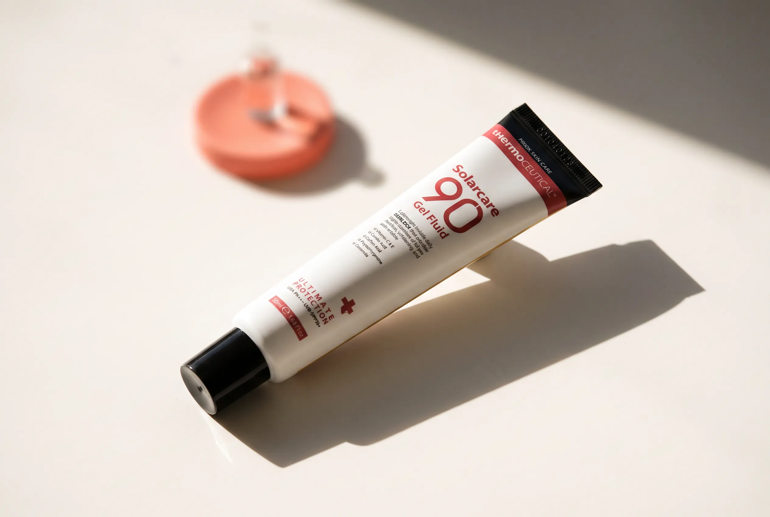 tHermoCEUTICAL Solarcare 90 Gel Fluid: weiße Tube mit rotem Etikett, schräg auf warmem Porzellanuntergrund im harten Morgenlicht, langer Schlagschatten